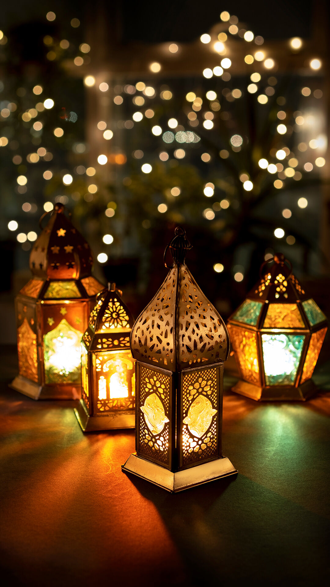 Two ornate metal lanterns with lit candles, casting a warm glow and light patterns on a surface.